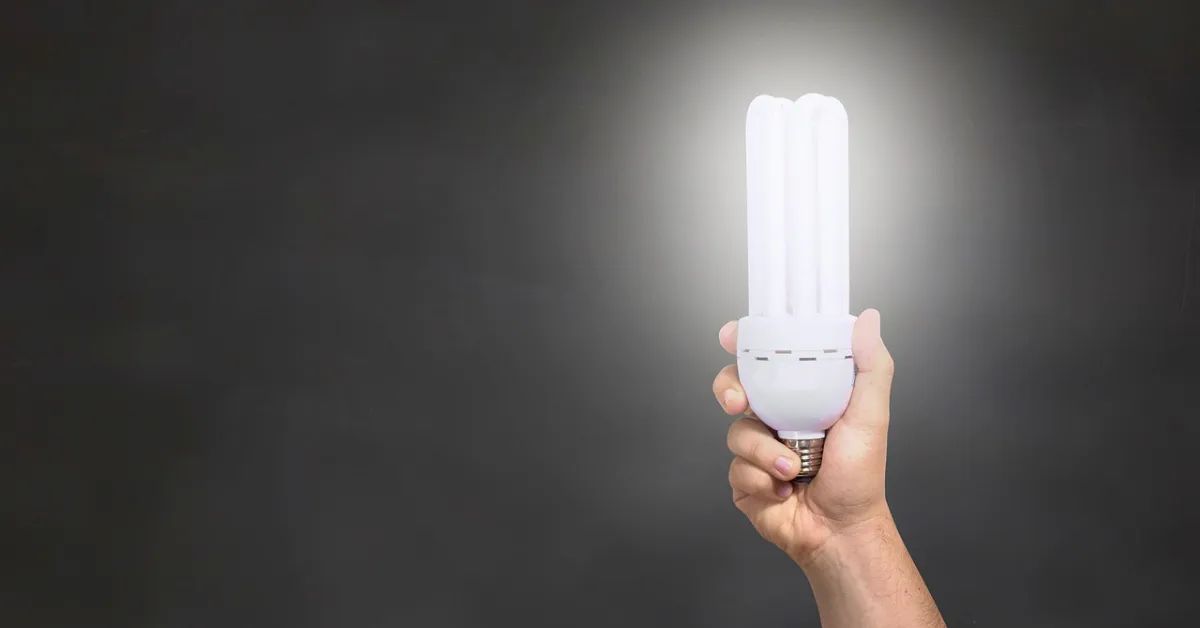 A hand holding a white light bulb with a black background