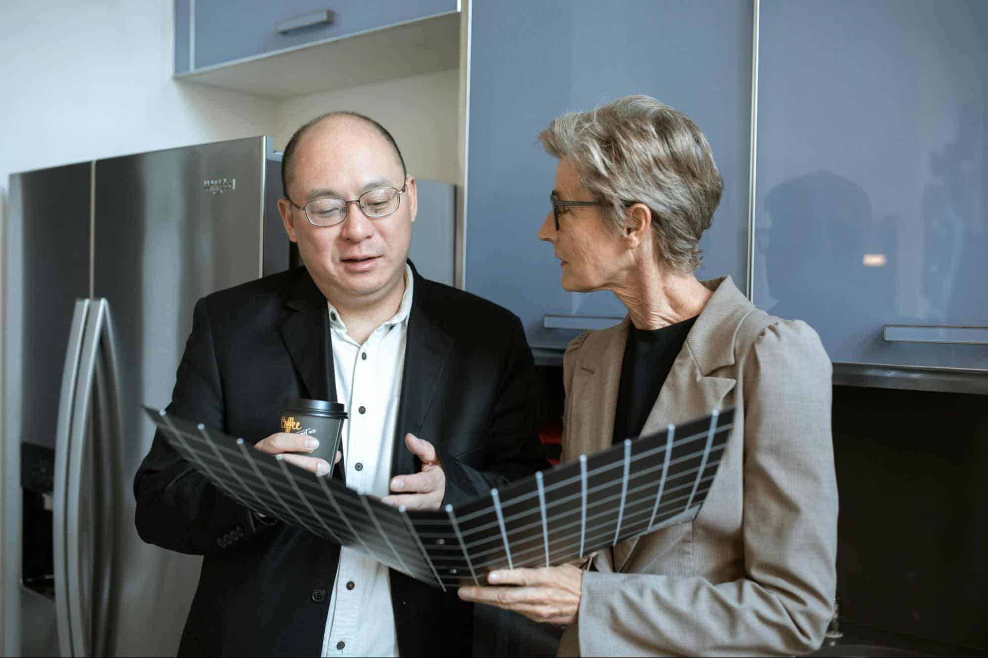 A man and woman in a kitchen with a fridge behind them.