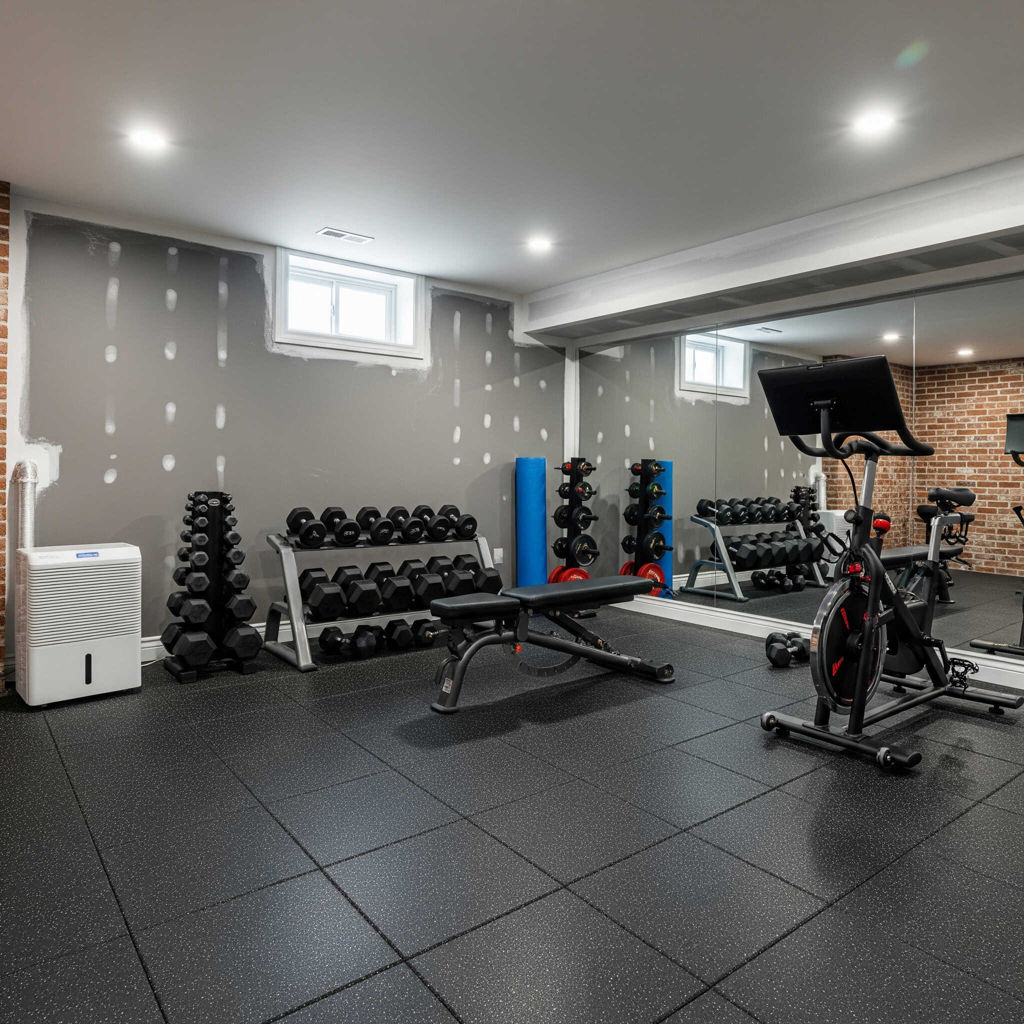 Well-lit basement gym with moisture-resistant flooring and a dehumidifier.