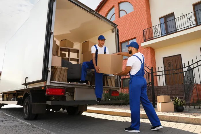 Bulk furniture removal workers carrying large household items into a truck for cheap same-day junk removal service near a residential home
