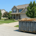 A worker in a high-visibility vest stands nearby, illustrating the scale of a standard residential waste container. This scene highlights the practical considerations of dumpster rental pricing and choosing the correct size for a home improvement project.