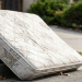 An old, worn mattress leaning against a suburban street curb, illustrating the need for easy, stress-free disposal services to avoid heavy lifting and hauling.