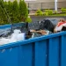 Blue roll-off dumpster filled with mixed trash and junk, showing local residential junk removal and trash hauling services available near me with affordable pricing and fast pickup.