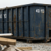 Image of a blue 40-yard roll-off dumpster on a gravel construction site, illustrating how big a 40 cubic yard dumpster is in terms of size dimensions and capacity. A text overlay provides a guide from JiffyJunk.com on rental costs and capacity to help you decide if this dumpster size is right for your project.