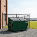 View of a large green 6 yard dumpster rental sitting on a gravel lot
