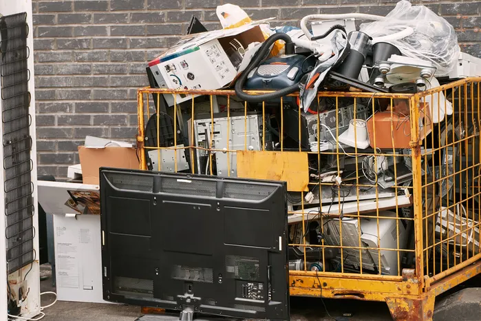An image of discarded TVs, computer towers, and small appliances in a metal cage for e-waste collection, showing how to recycle electronics responsibly