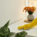 An image of hands wearing yellow cleaning gloves wiping a white surface during spring cleaning, illustrating a room by room deep cleaning and home decluttering checklist guide