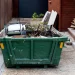 An image of a green dumpster filled with construction debris in a residential driveway.