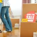 A view of packed moving boxes with a “home for sale” and “sold” sign inside a house, illustrating how to declutter before selling your home by organizing belongings, removing excess items, and preparing the space for staging to attract buyers and increase property value.
