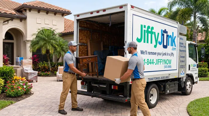 Two professional Jiffy Junk team members wearing branded Jiffy Blue and Jiffy Teal uniforms respectfully clear and carry household belongings from a residential property to a well-maintained, branded truck, delivering the White Glove Treatment for estate cleanout services in Naples, FL.