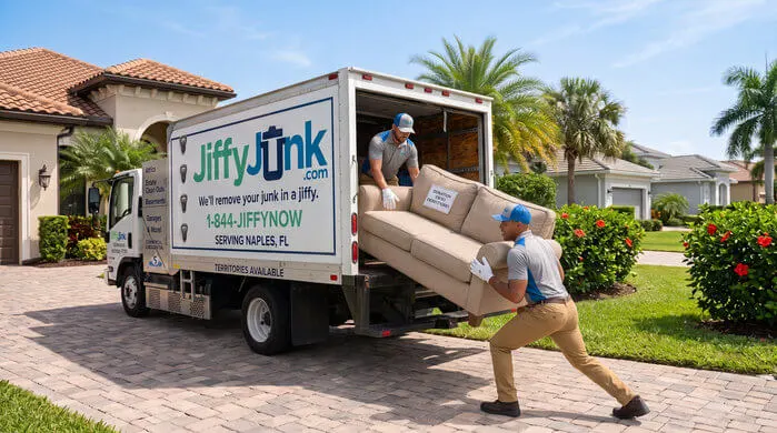 Two professional Jiffy Junk team members wearing branded Jiffy Blue and Jiffy Teal uniforms carefully carry a gently used sofa for donation toward a well-maintained, branded truck, delivering the White Glove Treatment for furniture donation services in Naples, FL.